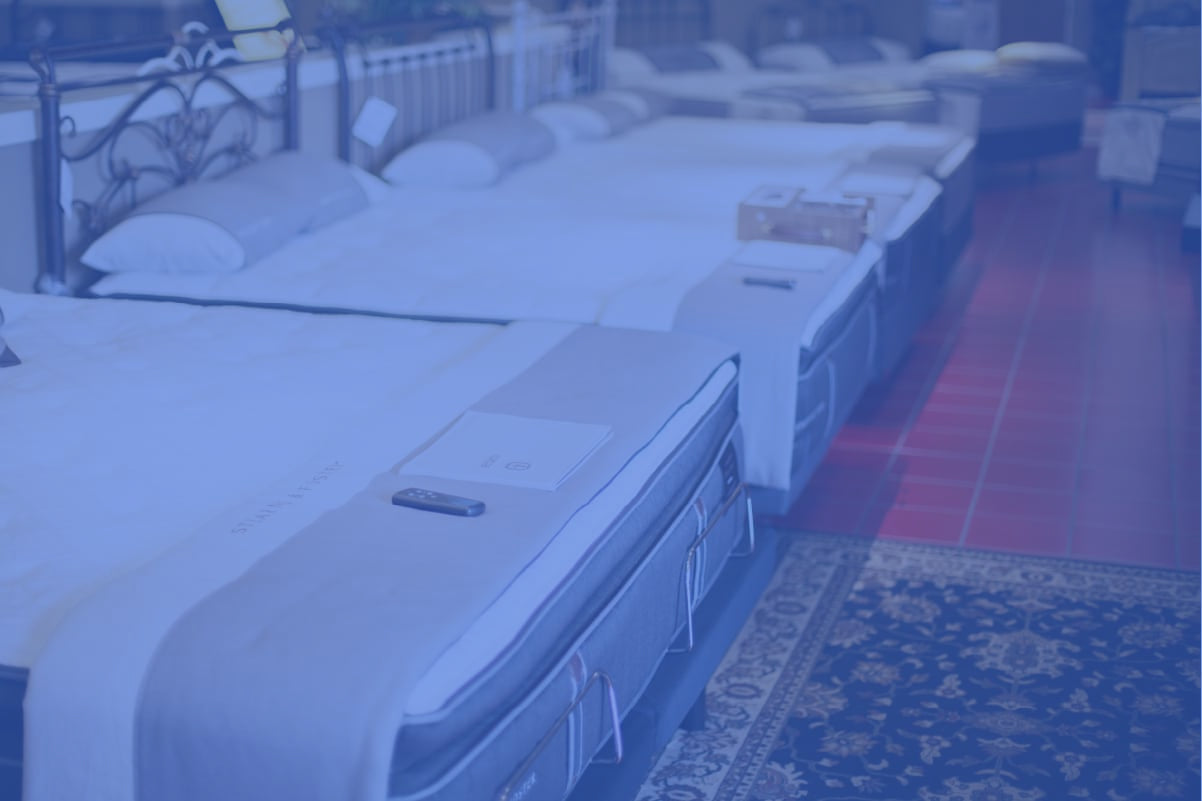 Mattresses on display in a showroom with red flooring and decorative rug.
